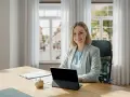 Uśmiechnięta kobieta w biurze przy biurku z tabletem i świnką-skarbonką.