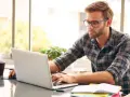 Mężczyzna w okularach pracuje przy laptopie, szukając informacji, jak zapłacić mandat przelewem Millenium.