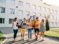 Pięcioro studentów idzie przed budynkiem uczelni, dyskutując o tym, jaki kredyt studencki jakie oprocentowanie będzie dla nich najlepsze.