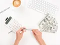 Kobieta planuje jak wypłacić pieniądze z funduszu inwestycyjnego ING, używając kalkulatora i notatnika. Obok leżą banknoty i filiżanka kawy.