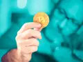 Dłoń trzymająca złoty bitcoin. Czy inwestowanie w kryptowaluty jest bezpieczne? Zastanawia się nad tym mężczyzna w okularach.