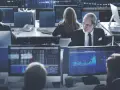 Ludzie w biurze analizują wykresy giełdowe na monitorach.