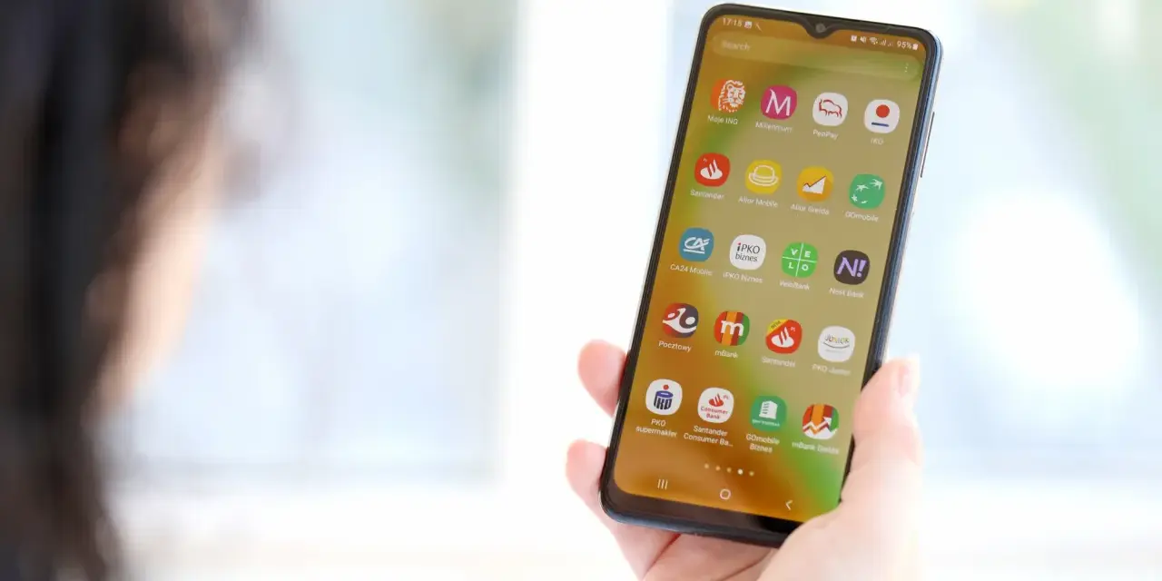 Dłoń trzyma smartfon z ikonami aplikacji bankowych. Widoczna ikona mBank, pomocna przy pytaniu jak zmienic numer telefonu mbank.