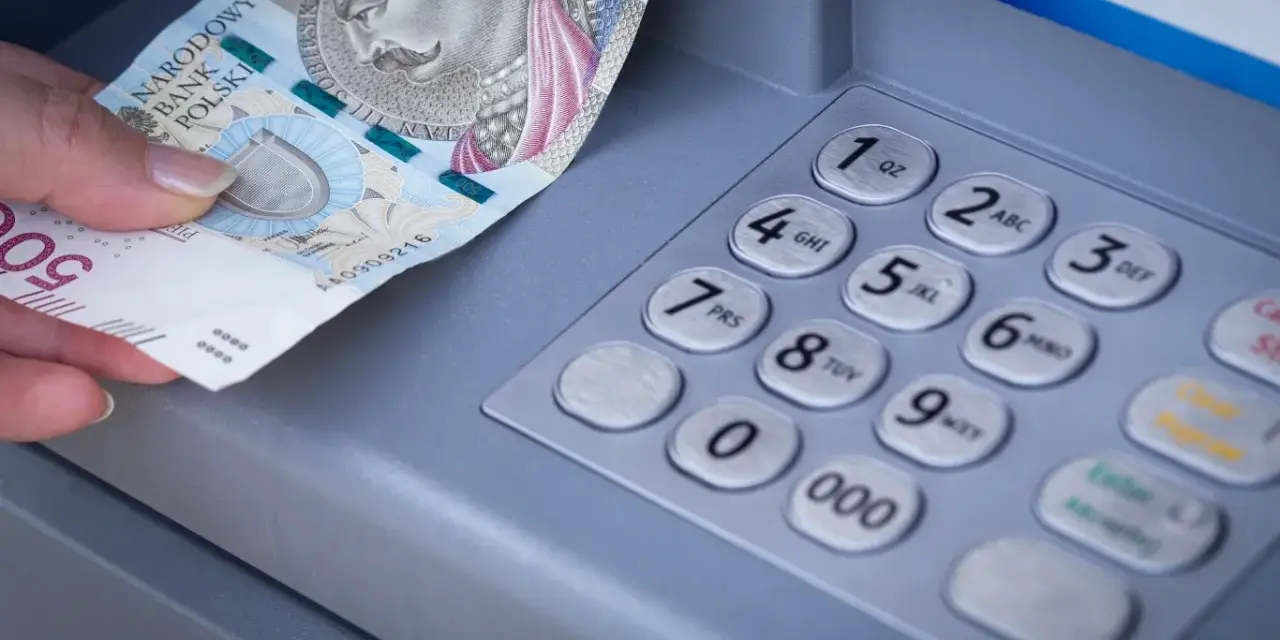 Dłoń z banknotem 500 zł przy bankomacie. Zastanawiasz się, przelew z mBanku do ING ile trwa?