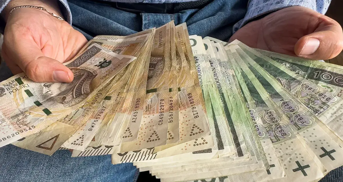 Dłonie trzymające plik polskich banknotów. Czy od pożyczki płaci się podatek? Pieniądze mogą być odpowiedzią.