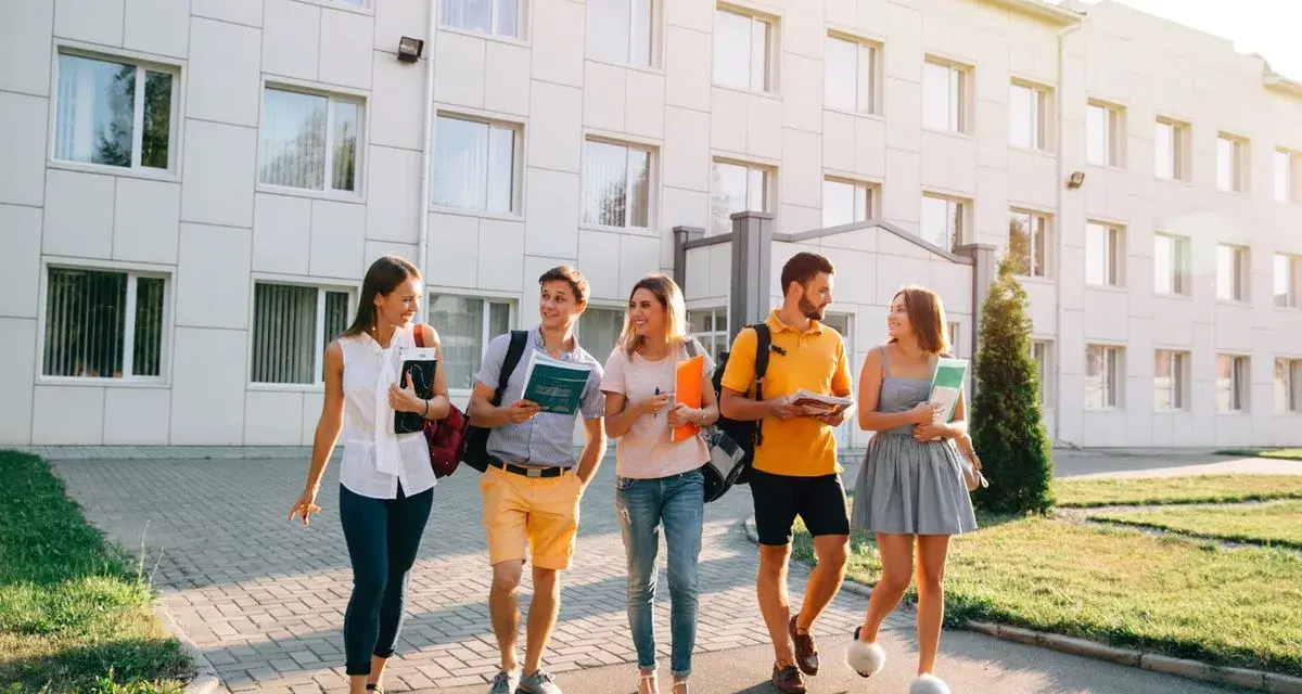 Pięcioro studentów idzie przed budynkiem uczelni, dyskutując o tym, jaki kredyt studencki jakie oprocentowanie będzie dla nich najlepsze.