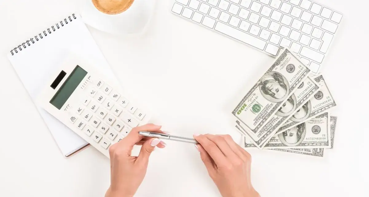 Kobieta planuje jak wypłacić pieniądze z funduszu inwestycyjnego ING, używając kalkulatora i notatnika. Obok leżą banknoty i filiżanka kawy.