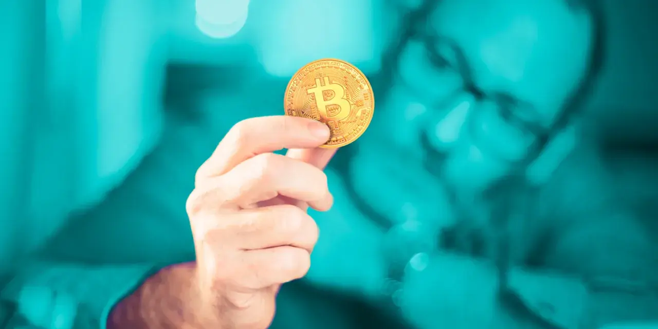 Dłoń trzymająca złoty bitcoin. Czy inwestowanie w kryptowaluty jest bezpieczne? Zastanawia się nad tym mężczyzna w okularach.