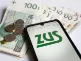 Złotówki i monety obok telefonu z logo ZUS. Pamiętaj o płaceniu składek, bo kto nie płaci funduszu pracy, ten ma problemy.