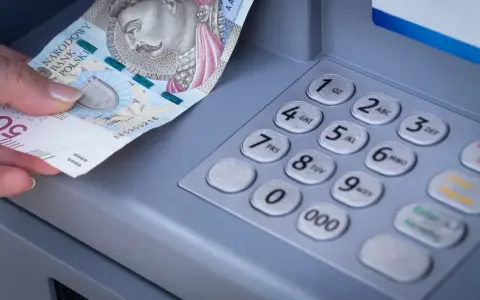 Dłoń z banknotem 500 zł przy bankomacie. Zastanawiasz się, przelew z mBanku do ING ile trwa?
