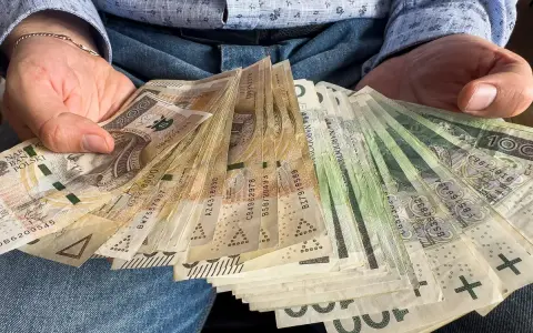 Dłonie trzymające plik polskich banknotów. Czy od pożyczki płaci się podatek? Pieniądze mogą być odpowiedzią.