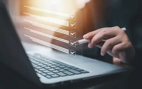 Ręka z długopisem zaznacza punkty na liście kontrolnej na ekranie laptopa. Proces ten może pomóc w ustaleniu, jak zmienić regulamin zakładowego funduszu świadczeń socjalnych.