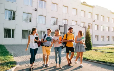 Pięcioro studentów idzie przed budynkiem uczelni, dyskutując o tym, jaki kredyt studencki jakie oprocentowanie będzie dla nich najlepsze.
