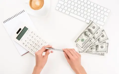Kobieta planuje jak wypłacić pieniądze z funduszu inwestycyjnego ING, używając kalkulatora i notatnika. Obok leżą banknoty i filiżanka kawy.