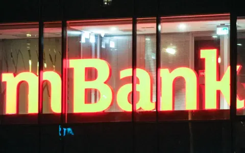 Jasne, oto propozycja tekstu alternatywnego:

Neonowy napis "mBank" świeci w nocy. To bank, do którego należą miliony Polaków, oferujący nowoczesne usługi finansowe.
