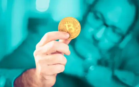 Dłoń trzymająca złoty bitcoin. Czy inwestowanie w kryptowaluty jest bezpieczne? Zastanawia się nad tym mężczyzna w okularach.