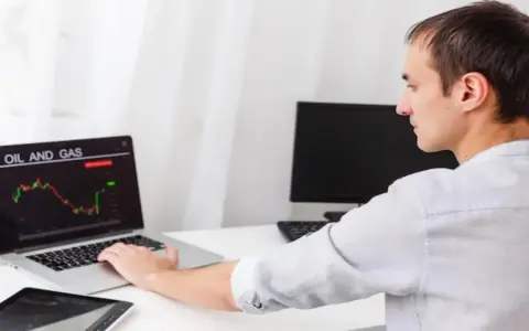 Mężczyzna analizuje wykres cen ropy i gazu na laptopie.