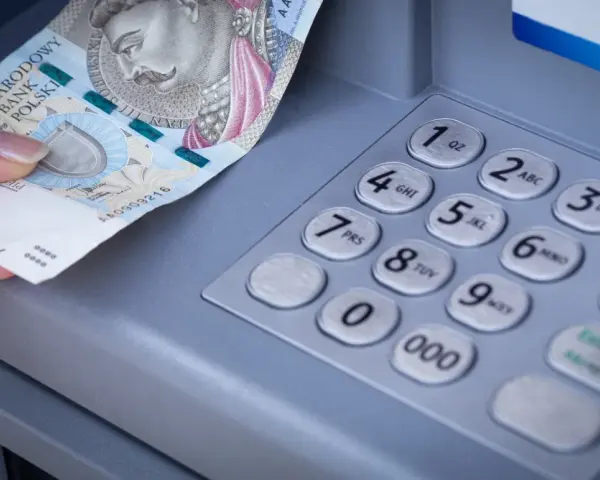 Dłoń z banknotem 500 zł przy bankomacie. Zastanawiasz się, przelew z mBanku do ING ile trwa?