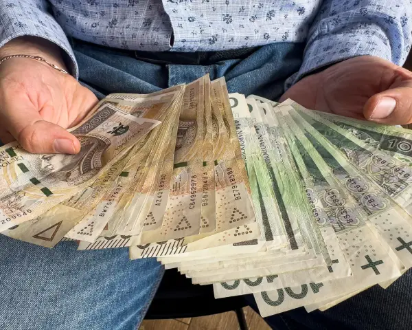 Dłonie trzymające plik polskich banknotów. Czy od pożyczki płaci się podatek? Pieniądze mogą być odpowiedzią.