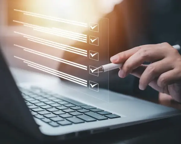 Ręka z długopisem zaznacza punkty na liście kontrolnej na ekranie laptopa. Proces ten może pomóc w ustaleniu, jak zmienić regulamin zakładowego funduszu świadczeń socjalnych.