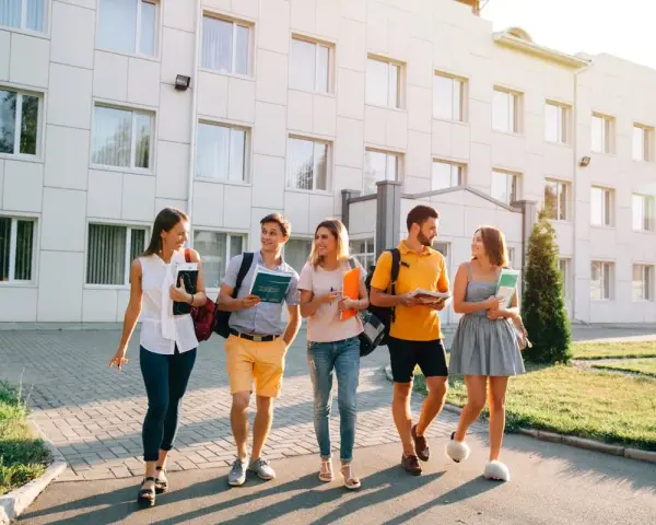 Pięcioro studentów idzie przed budynkiem uczelni, dyskutując o tym, jaki kredyt studencki jakie oprocentowanie będzie dla nich najlepsze.