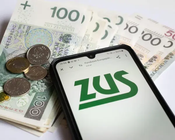 Złotówki i monety obok telefonu z logo ZUS. Pamiętaj o płaceniu składek, bo kto nie płaci funduszu pracy, ten ma problemy.