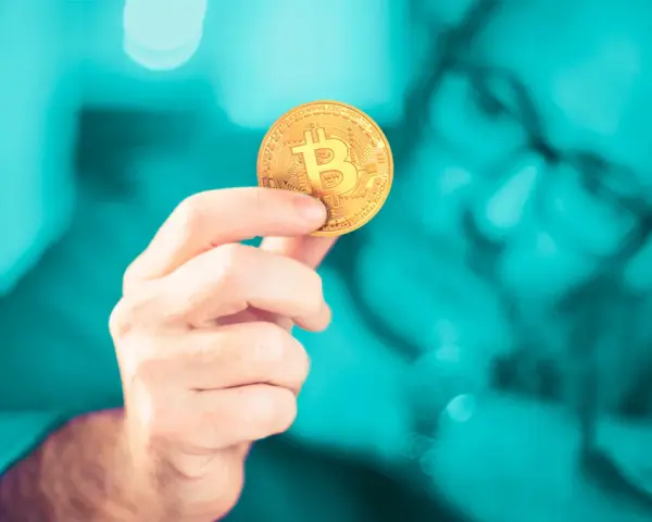 Dłoń trzymająca złoty bitcoin. Czy inwestowanie w kryptowaluty jest bezpieczne? Zastanawia się nad tym mężczyzna w okularach.