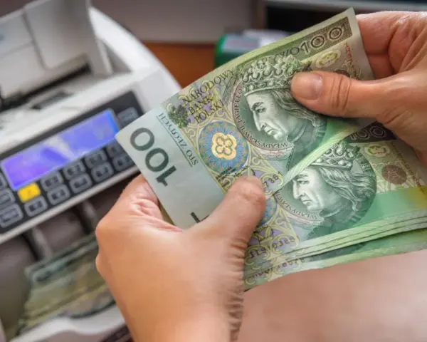 Ręce trzymają banknoty 100 zł obok licznika pieniędzy. Czy przy wcześniejszej spłacie kredytu należy się zwrot odsetek?
