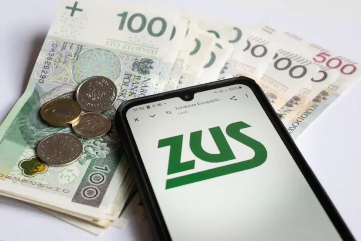 Złotówki i monety obok telefonu z logo ZUS. Pamiętaj o płaceniu składek, bo kto nie płaci funduszu pracy, ten ma problemy.
