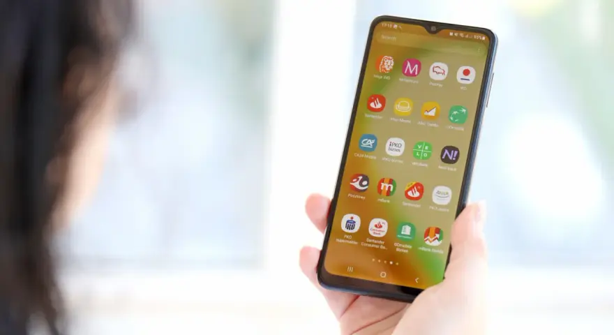 Dłoń trzyma smartfon z ikonami aplikacji bankowych. Widoczna ikona mBank, pomocna przy pytaniu jak zmienic numer telefonu mbank.