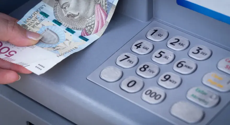 Dłoń z banknotem 500 zł przy bankomacie. Zastanawiasz się, przelew z mBanku do ING ile trwa?