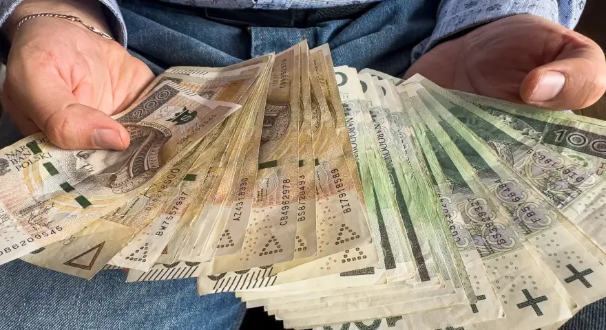 Dłonie trzymające plik polskich banknotów. Czy od pożyczki płaci się podatek? Pieniądze mogą być odpowiedzią.