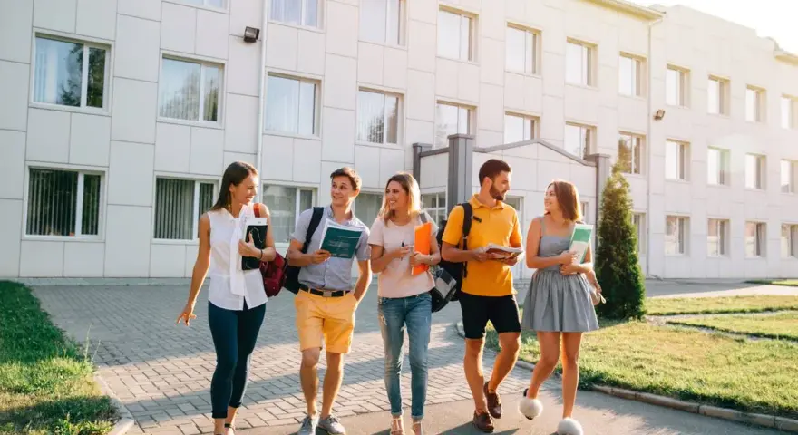 Pięcioro studentów idzie przed budynkiem uczelni, dyskutując o tym, jaki kredyt studencki jakie oprocentowanie będzie dla nich najlepsze.