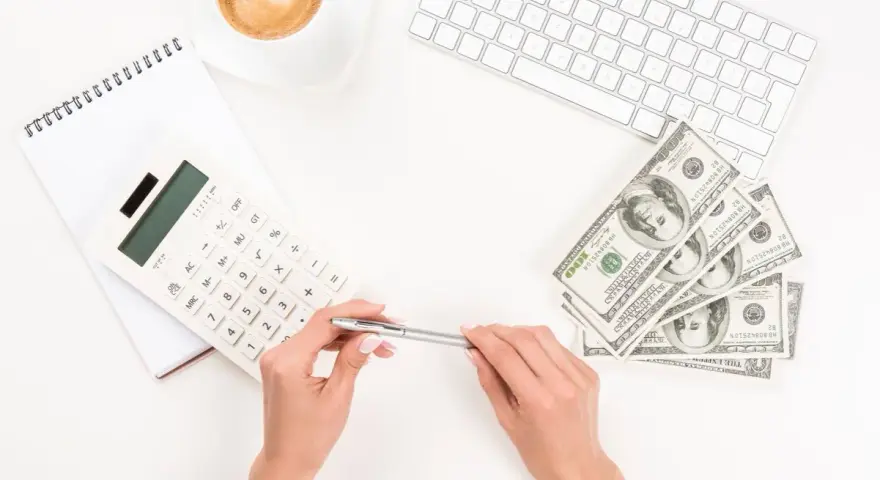 Kobieta planuje jak wypłacić pieniądze z funduszu inwestycyjnego ING, używając kalkulatora i notatnika. Obok leżą banknoty i filiżanka kawy.