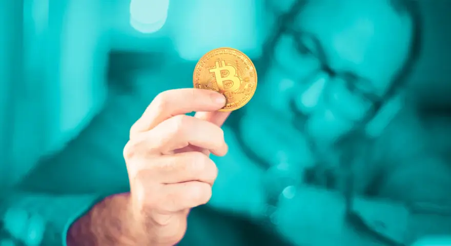 Dłoń trzymająca złoty bitcoin. Czy inwestowanie w kryptowaluty jest bezpieczne? Zastanawia się nad tym mężczyzna w okularach.
