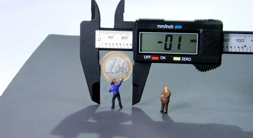 Figurki ludzi mierzą monetę suwmiarką, symbolizując, jak obliczyć odsetki od pożyczki.