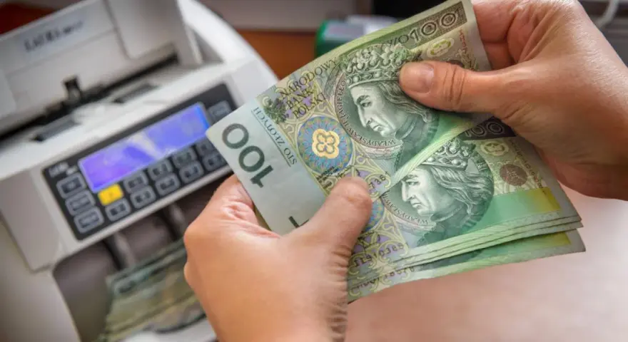 Ręce trzymają banknoty 100 zł obok licznika pieniędzy. Czy przy wcześniejszej spłacie kredytu należy się zwrot odsetek?