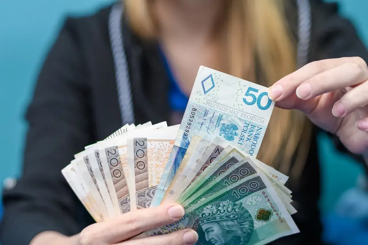 Ręce trzymające plik polskich banknotów. Czy Revolut sprawdza BIK? Pieniądze mogą być potrzebne na spłatę zobowiązań.