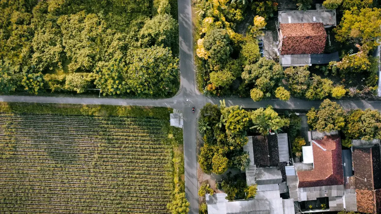 Widok z lotu ptaka na skrzyżowanie dróg, pola uprawne i domy. To może być działka inwestycyjna, co to znaczy? Potencjał rozwoju.