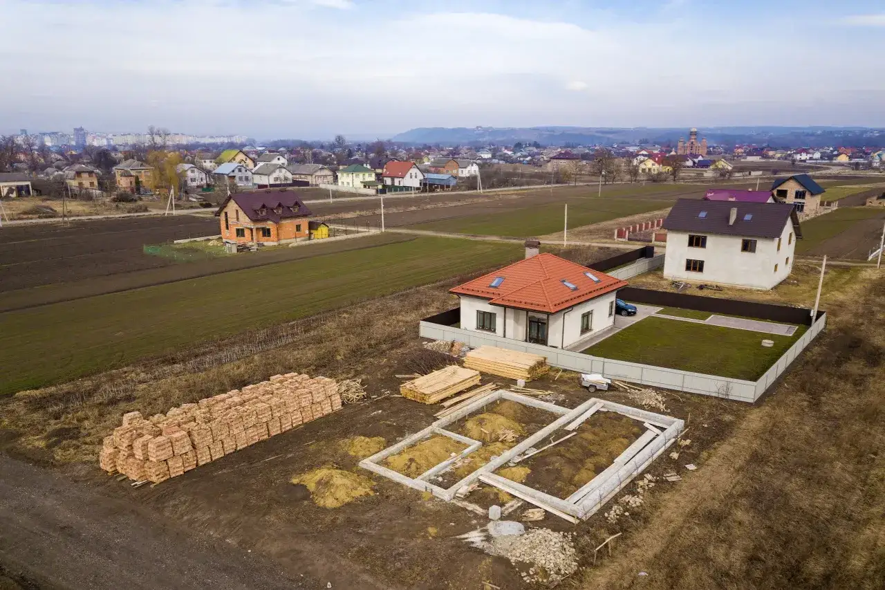 Działka inwestycyjna co to znaczy? Widok z lotu ptaka na osiedle domów w budowie, z fundamentami, stertami cegieł i drewna.